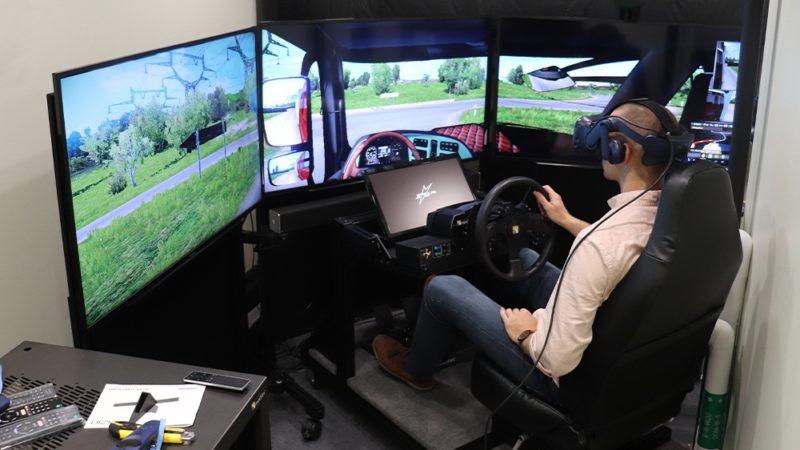 man wearing a headset seated in front of three screens simulating driving an autonomous vehicle