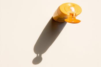 bottle of yellow sunscreen casting a shadow against a white table