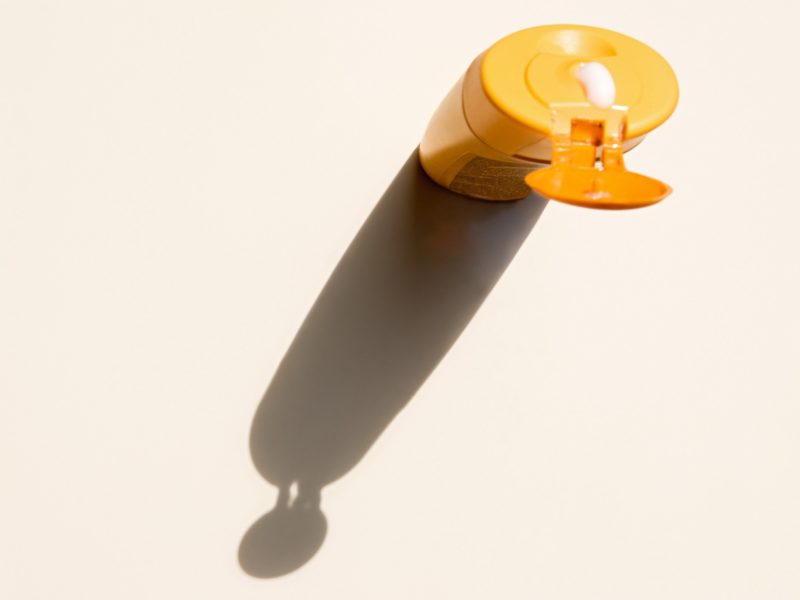 bottle of yellow sunscreen casting a shadow against a white table