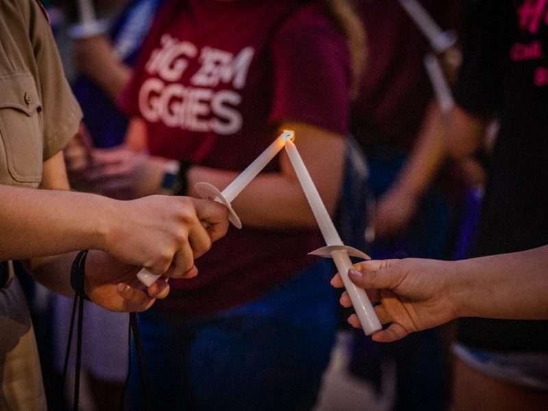 close up image of a student using a white candle to hold a candle held by another person