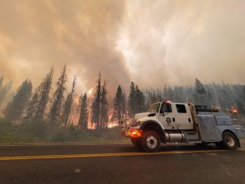 a photo of a firetruck in front of a raging forest fire