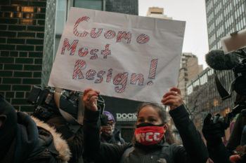 a woman holds a sign that says "Cuomo must resign!"