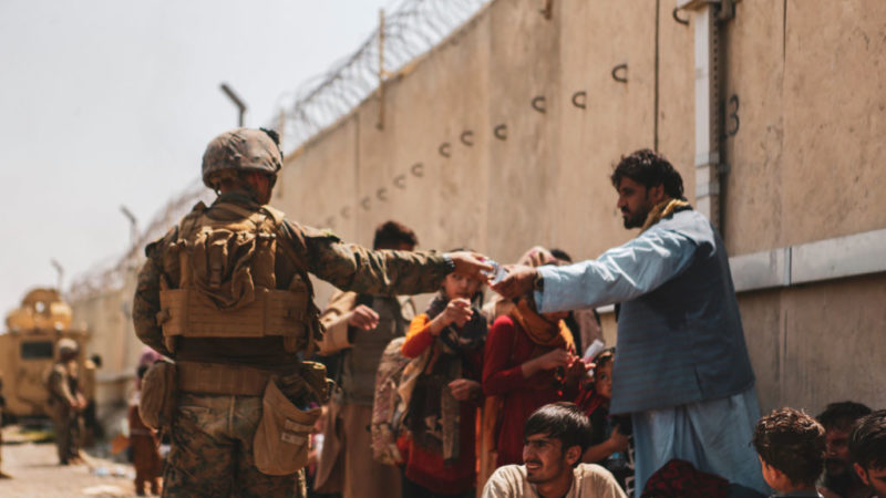 soldier hands out water to afghan evacuees outside an airport