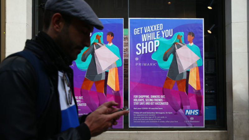 a man walks past a sign advertising in-store vaccinations at a store in london