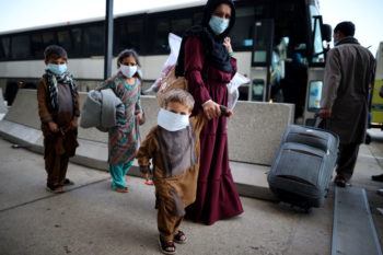 afghan man holds the hands of young children as she boards a bus