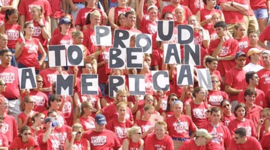 the crowd wearing red at the original RWB game holding signs that spell out Proud to be an American