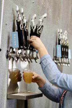 cropped images of a woman's hand's at beer taps, with one hand filling a cup with beer