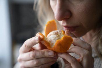 close up image of a woman smelling a peeled orange