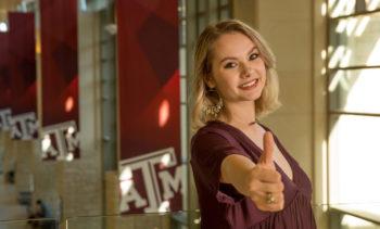 portrait of natalie parks in the memorial student center giving a gig 'em sign to camera