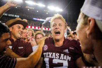 crowd of fans surround a football player in a texas a&m jersey