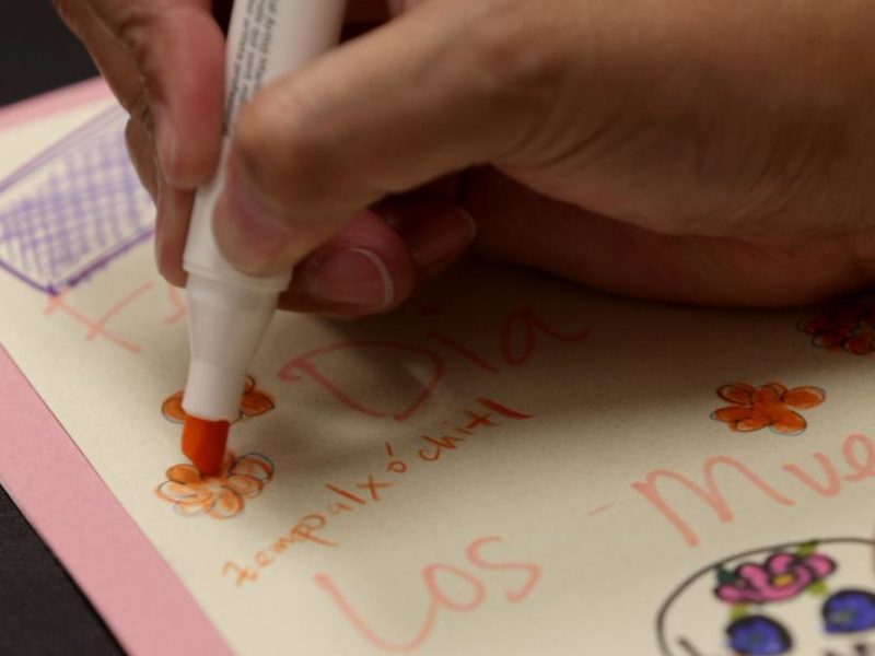 close up image of a students hand holding an orange marker as they decorate a piece of paper with orange flowers