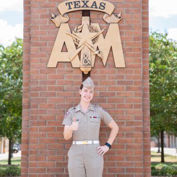 a photo of Amanda Lovitt in her Corps uniform giving the gig 'em thumb, standing in the Quad