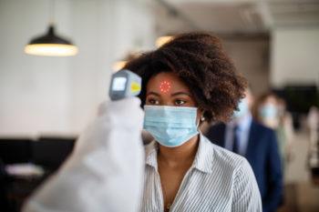 Woman wearing protective mask goes through a temperature checks before going to work in the office.