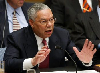 colin powell gestures with hands while seated before a microphone