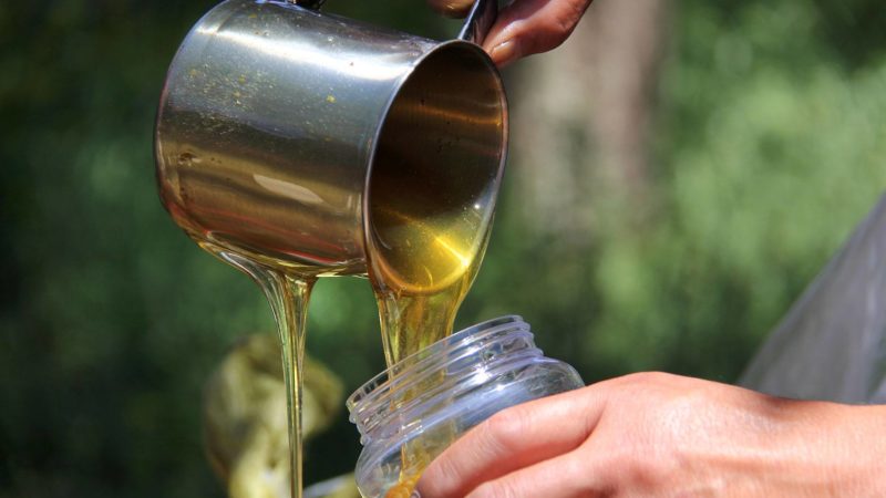 close up image of someone pouring honey into a glass jar