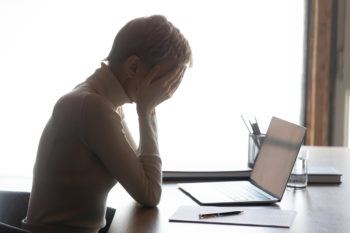 a woman holding her head in her hands sitting in front of a laptop