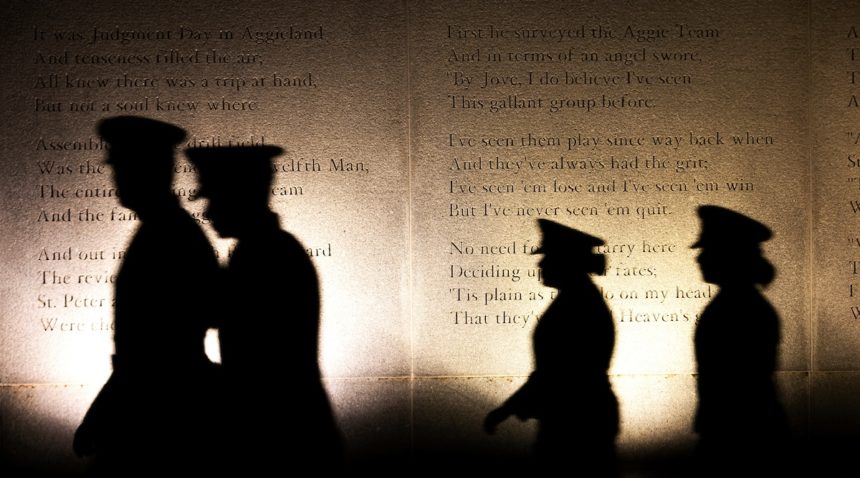 silhouttes of cadets walking past a large granite wall engraved with a poem