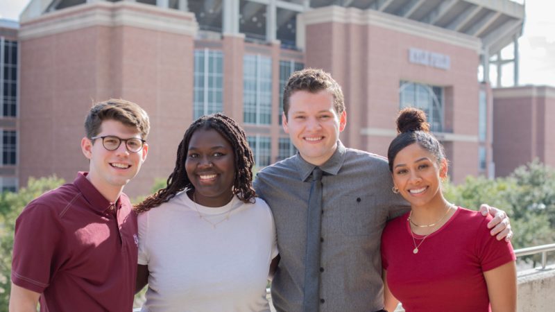 group photo of four students standing in front of kyle field