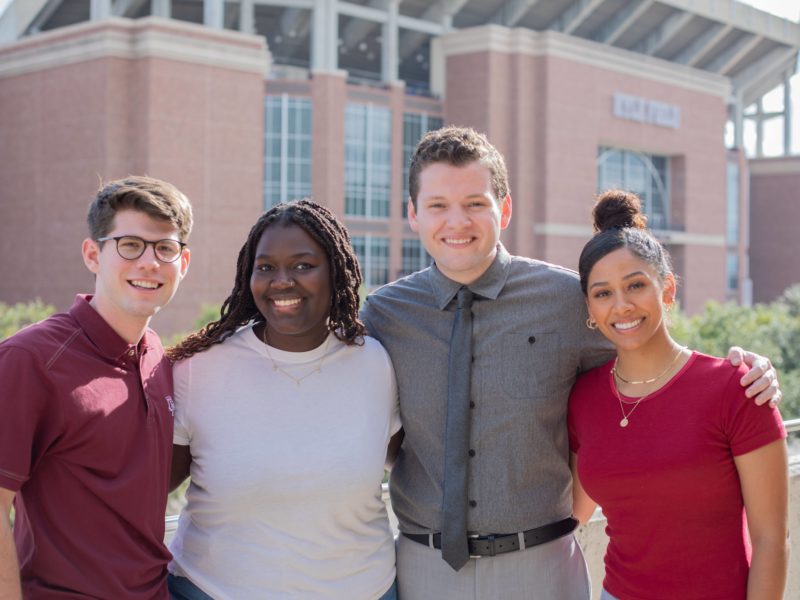 group photo of four students standing in front of kyle field