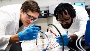 two men in lab equipment work on experiment involving wires