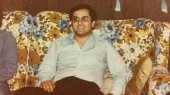 photo of man sitting on a floral print couch wearing an aggie ring
