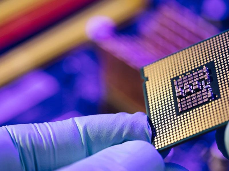 close up of a person wearing purple gloves holding a computer chip