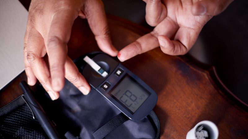 cropped shot of the hands of a person using a blood sugar testing device on one finger