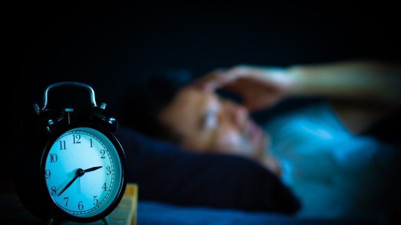 man laying in bed awake next to alarm clock in the middle of the night