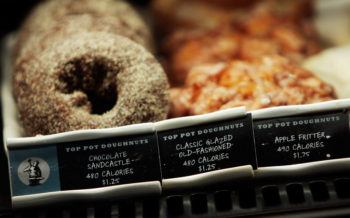 different kinds of donuts are displayed in a case, with small black labels below them listing the calorie content