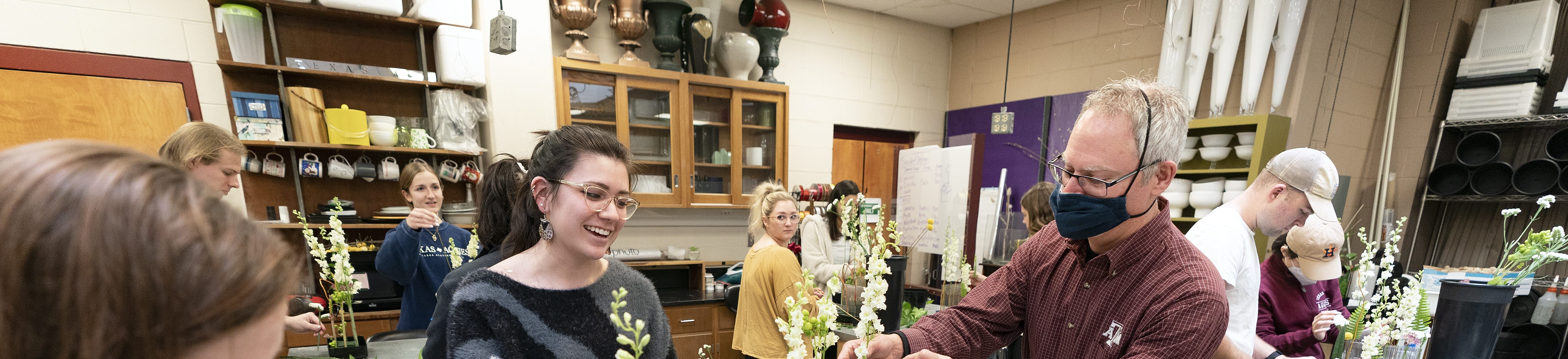 a professor and students stand around a table working on floral arrangements