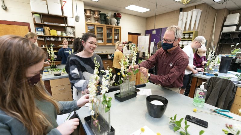 a professor and students stand around a table working on floral arrangements