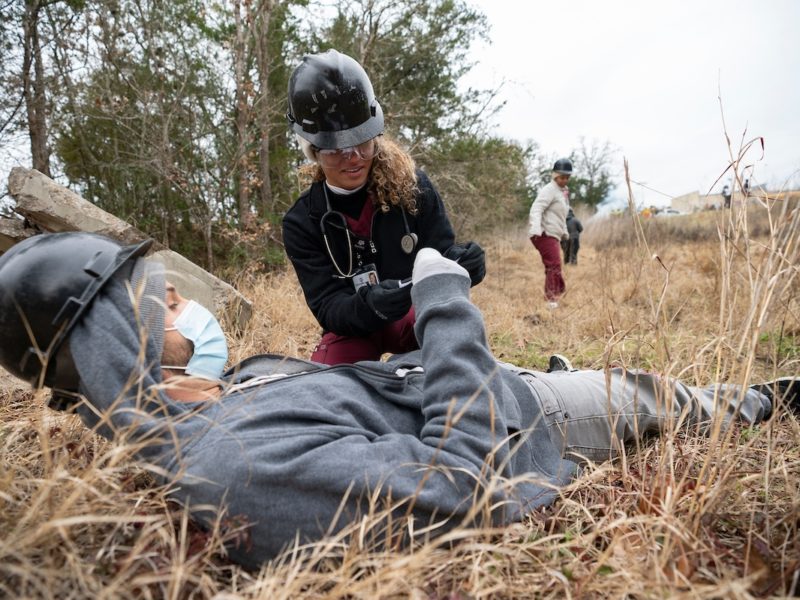 a female student kneels next to a male student in a field during a wildfire simulation