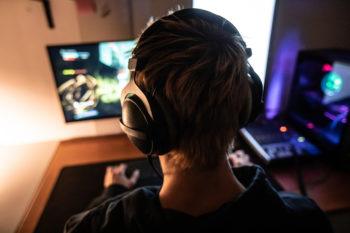 rear view of a gamer with a headset on facing a computer monitor where he plays video games