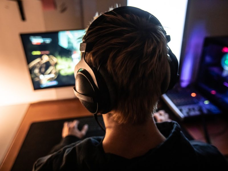 rear view of a gamer with a headset on facing a computer monitor where he plays video games