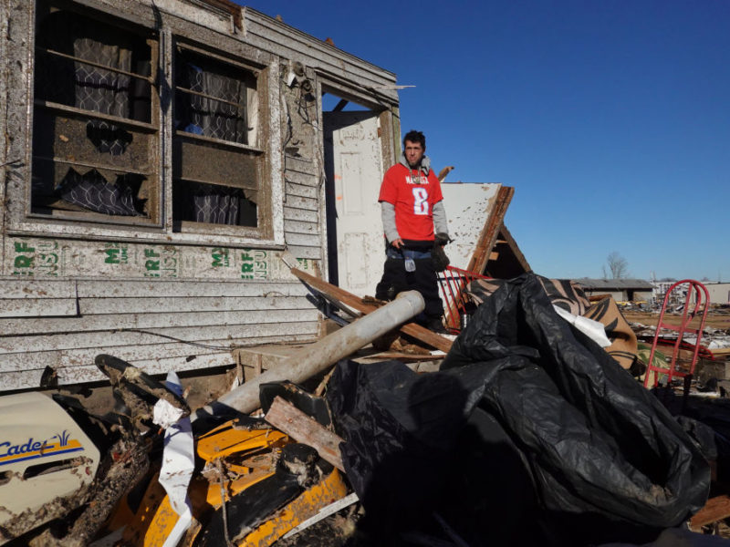 a man stands on the porch in front of a house destroyed by a tornado