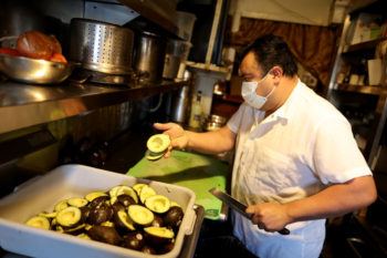 a chef in a restaurant kitchen prepares avocados to be made into guacamole