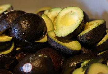 pile of fresh avocados in a bowl, with some cut in half