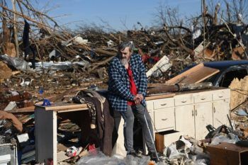 a man sits on a piece of furniture in the middle of a pile of rubble in a destroyed neighborhood