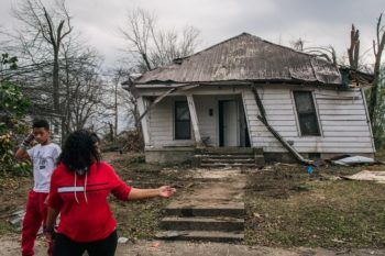 a woman looks back toward a home damaged after a tornado