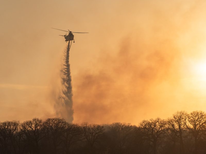 silhouette of a helicopter dumpin gwater over a wildfire against an orange sunset