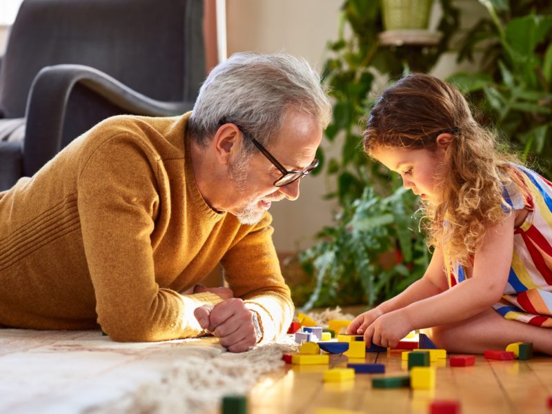 child playing with blocks on the floor next to a grandparent