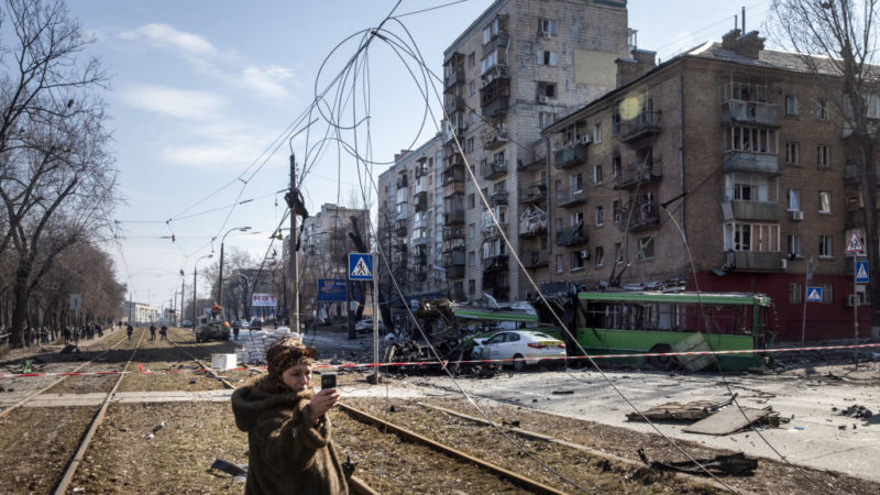 A woman takes a selfie in front of a damaged residential apartment block caused after a Russian rocket was shot down by Ukrainian air defences