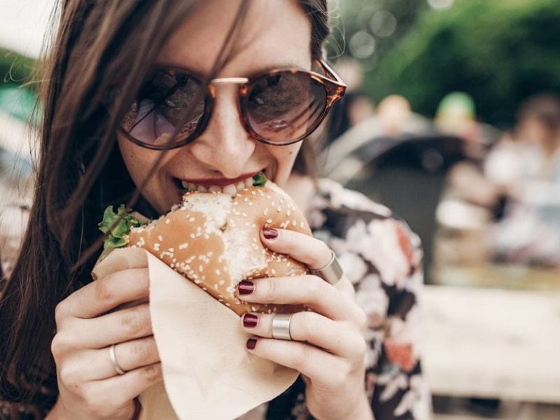 woman dining outdoors biting into a hamburger