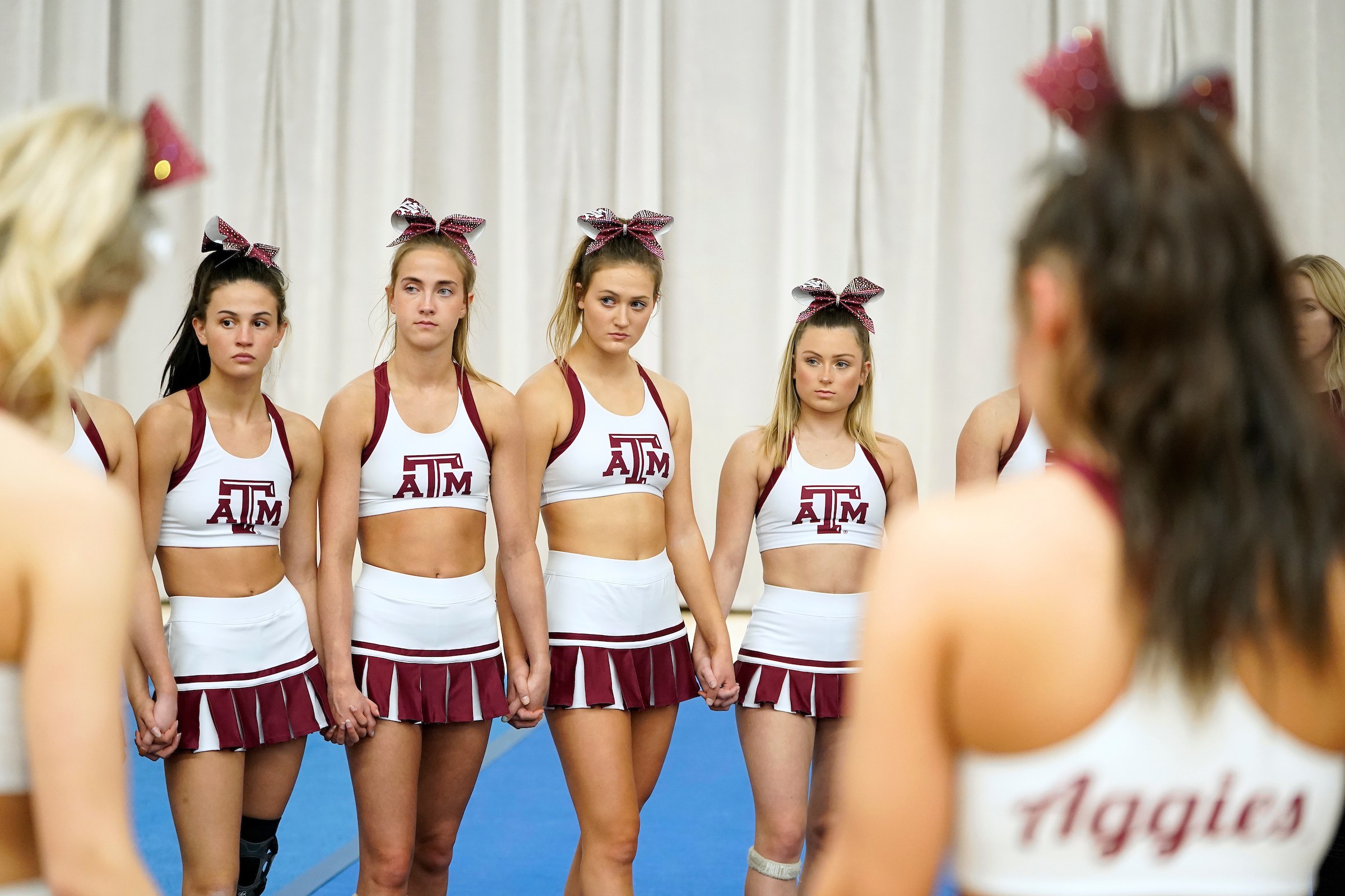 a group of cheerleaders stands in a circle holding hands in front of a curtain