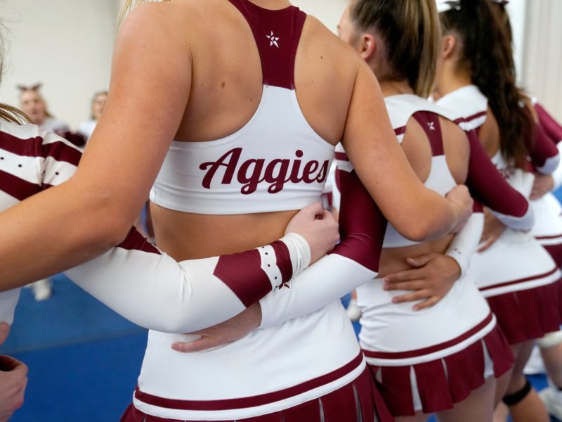 a photo of the backs of several cheerleaders who are standing in a circle with their arms around each other
