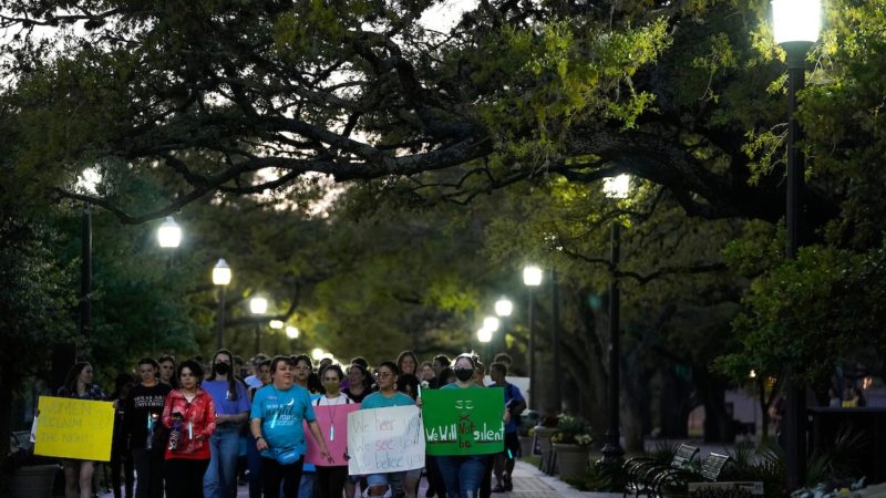 a large group of students walk through campus at night holding signs