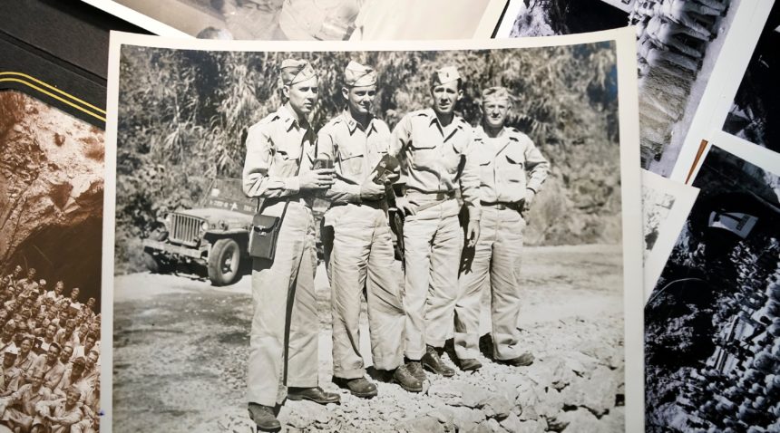 a black and white photo of four men in army uniforms sits on top of an assortment of other old photographs on a table