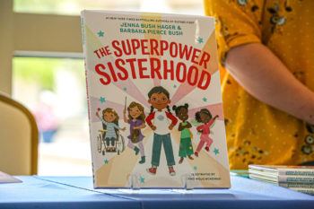a children's book propped up on a table. the title reads "the superpower sisterhood."