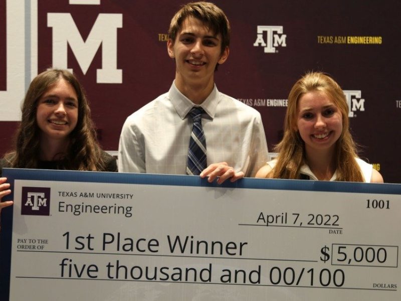 three students hold an oversized check for their first place win, with a $5,000 total