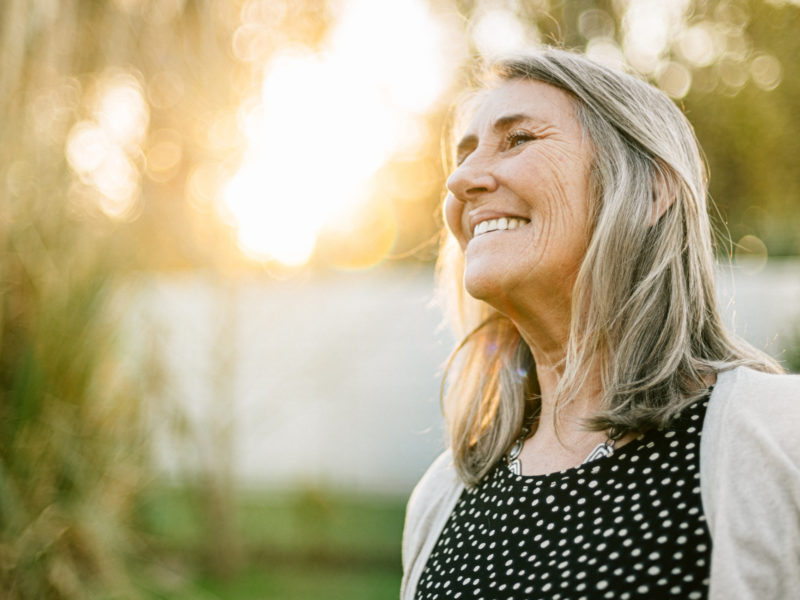 portrait of a senior woman smiling outdoors with a sunset behind her